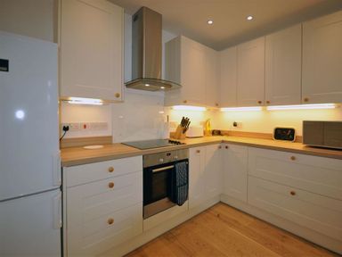 A kitchen with white cabinets wooden countertops a refrigerator an oven stovetop a knife block a microwave and under cabinet lighting at Pebbles in Burton Bradstock