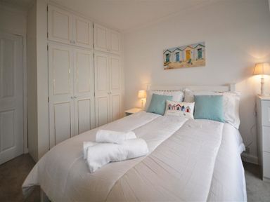A bedroom with a bed white bedding two lamps and built-in white wardrobes at Pebbles in Burton Bradstock