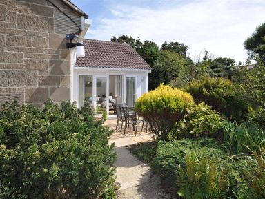 A garden patio with outdoor furniture and sliding glass doors leading to a living room at Pebbles in Burton Bradstock