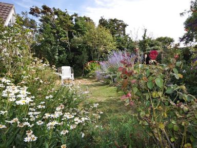 A garden with flowers trees and a white chair at Pebbles in Burton Bradstock