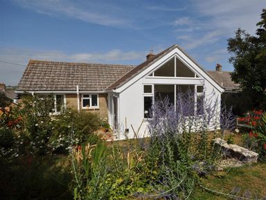 A house with a tiled roof and large windows surrounded by a garden with various plants and flowers at Pebbles in Burton Bradstock