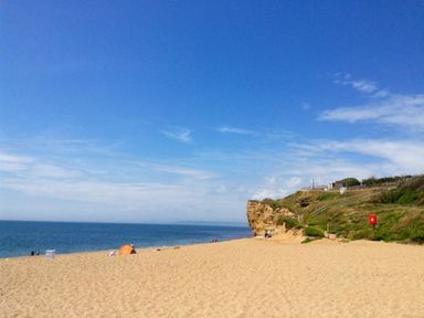 A sandy beach with a few people tents near the shoreline and a grassy cliff at Pebbles Burton Bradstock