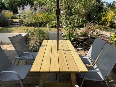 A table with chairs under an umbrella in a garden at Pebbles in Burton Bradstock