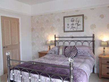A bedroom with a metal bed frame, patterned bedding, two bedside tables with lamps and a framed artwork on the wall at Pedaller's Cottage in Weymouth