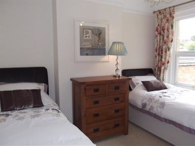 A bedroom with two single beds a wooden chest of drawers and a lamp at Pedaller's Cottage in Weymouth