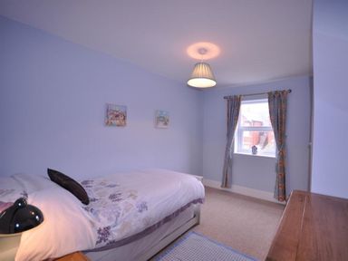 A bedroom with a single bed a window with curtains and a wooden dresser at Pedaller's Cottage in Weymouth