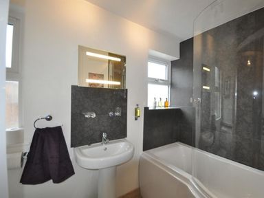 A bathroom with a sink, mirror, towel holder, bathtub, and toiletries at Pedaller's Cottage in Weymouth