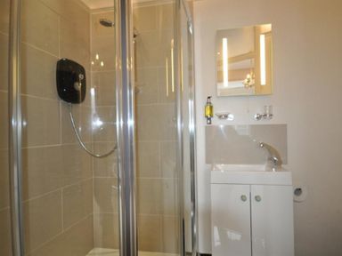 A bathroom with a shower enclosure and a sink with a mirror above at Pedaller's Cottage in Weymouth