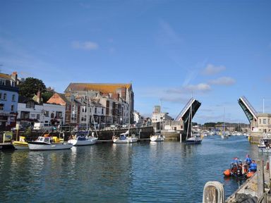 A harbor with boats docked next to buildings and a raised drawbridge at Pedaller's Cottage in Weymouth