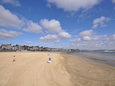 A sandy beach with two children playing near the shore and buildings in the background at Pedaller's Cottage in Weymouth