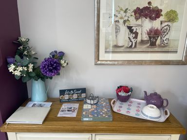 A table with flowers, books, a teapot, and a picture at Pedaller's Cottage in Weymouth