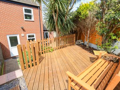 A wooden deck with a bench and small table next to a garden with trees and plants at The Pines in Weymouth