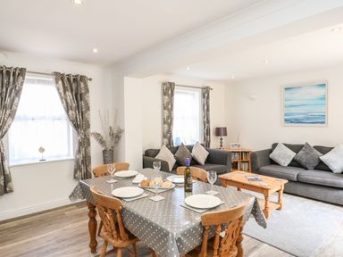 A dining table set with plates and wine bottle beside two sofas with cushions in a living room at The Pines in Weymouth