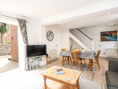 A living room with a dining table set for four a coffee table and a TV near a sliding door at The Pines in Weymouth