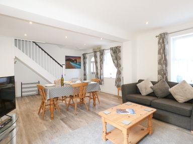 A living room and dining area with a gray sofa, wooden dining table with chairs, and a wooden coffee table at The Pines in Weymouth