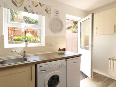 A kitchen with a sink washing machine dishwasher fruit bowl and open door at The Pines in Weymouth