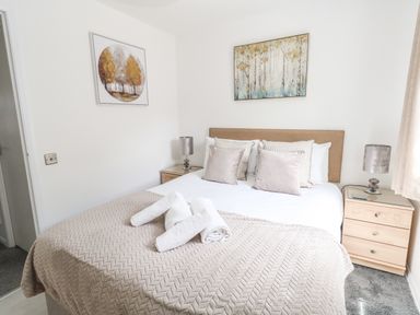 A bedroom with a bed with pillows and rolled towels bedside tables with lamps and paintings on the walls at The Pines in Weymouth