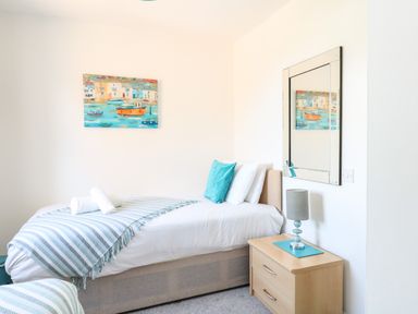 A bedroom with a single bed with striped bedding two white rolled towels a bedside table with a lamp and a wall mirror at The Pines in Weymouth