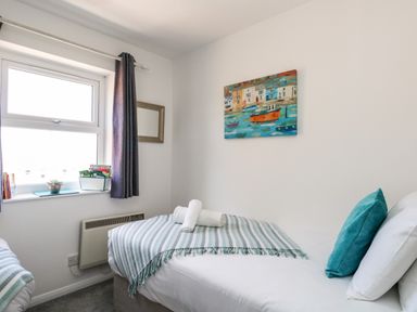 A bedroom with a single bed with white linens and blue striped blanket near a window with dark curtains at The Pines in Weymouth
