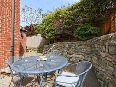 A patio area with metal table and chairs with glasses and cupcakes next to a brick wall and stone retaining wall at The Pines in Weymouth