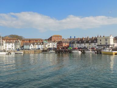 A harbor with boats docked along a waterfront with buildings and cars at The Pines in Weymouth