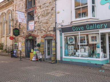 A street view showing Londis Harbour Stores and Cove Gallery with various signs and items displayed outside at The Pines in Weymouth