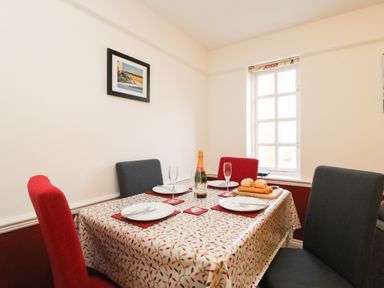 A dining room with a table set with plates wine glasses bread and a bottle with chairs at Poppies in Brewers Quay Harbour