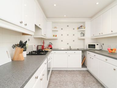 A kitchen with white cabinets grey countertops tiled floor and various appliances at Poppies Brewers Quay Harbour