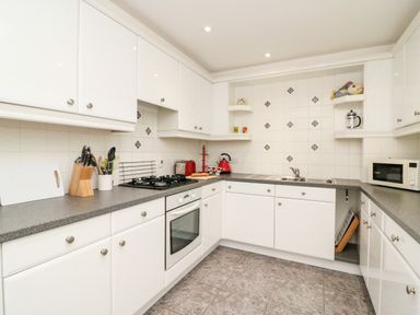 A kitchen with white cabinets a gas stove knife block microwave and tiled walls at Poppies Brewers Quay Harbour