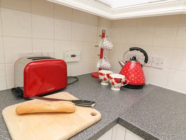 A kitchen counter with a red toaster a cutting board with a bread loaf and knife a red kettle with white polka dots two cups with red flowers and a cup holder at Poppies Brewers Quay Harbour