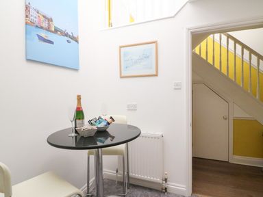 A small dining area with a round table two chairs a bottle of champagne and snacks on the table a radiator on the wall and stairs with yellow wall paneling at Poppies Brewers Quay Harbour