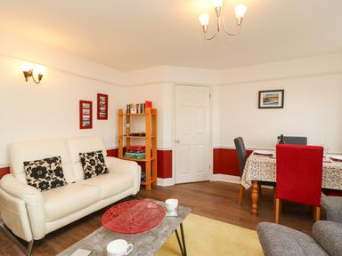 A living room with a white sofa black patterned cushions a wooden bookshelf and a dining table with red and gray chairs at Poppies Brewers Quay Harbour