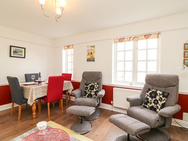 A room with dining table and chairs and two reclining armchairs with cushions at Poppies Brewers Quay Harbour