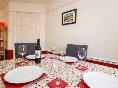 A dining table with four place settings and a bottle of wine in a room with a white door and framed picture at Poppies Brewers Quay Harbour