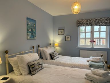 A bedroom with two single beds and pillows with house designs at Poppies in Brewers Quay Harbour