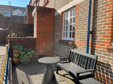 An outdoor patio area with a black bench table potted plants and brick walls at Poppies in Brewers Quay Harbour