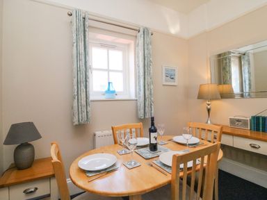 A dining room with a wooden table set for four with plates glasses a blue vase on the window sill and two lamps at Reaver Brewers Quay harbour