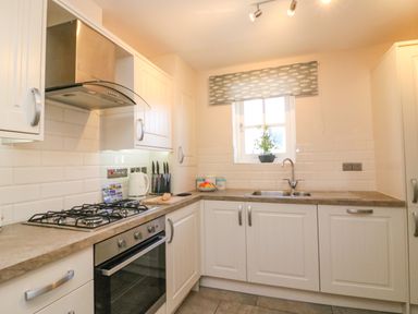 A kitchen with white cabinets a stove a sink and a small window with a patterned blind at Reaver Brewers Quay harbour