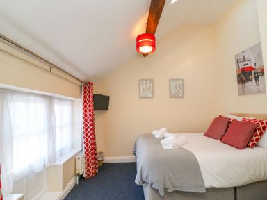 A bedroom with a bed with towels on it red and white curtains and a wall-mounted television at Reaver Brewers Quay harbour