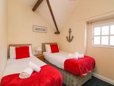 A bedroom with two single beds with red blankets and pillows a nightstand with a lamp and a window at Reaver Brewers Quay harbour