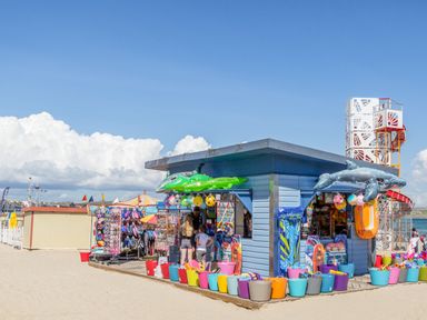 A beach shop selling inflatables toys buckets and beach accessories on a sandy beach with a play structure in the background at Brewers Quay harbour