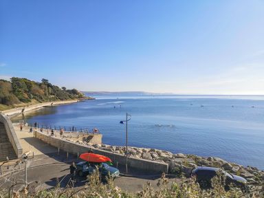 A coastal walkway with people near a sea wall and kayaks on a car at Reaver Brewers Quay harbour