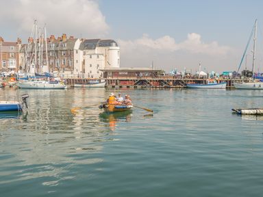 People in a small rowboat on water with sailboats and buildings in the background at Brewers Quay harbour