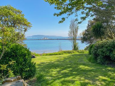 A grassy area with trees and bushes overlooking a body of water with distant land and buildings at Brewers Quay harbour