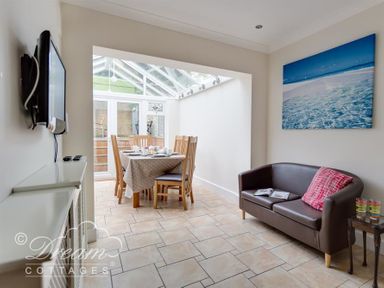 A dining area with a table and chairs next to a brown sofa with a red pillow and a wall-mounted television at Redcliff View Lodge in Weymouth