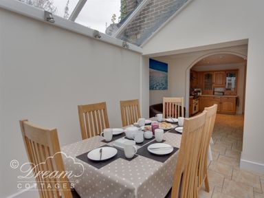 A dining area with a table set for six and wooden chairs next to a kitchen at Redcliff View Lodge in Weymouth