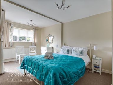 A bedroom with a turquoise bedspread on a bed two white chairs by a window and a white dresser at Redcliff View Lodge in Weymouth