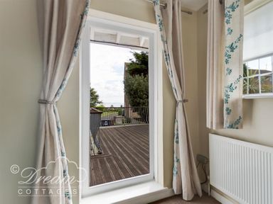 A room with curtains on either side of a glass door leading to a wooden deck outside at Redcliff View Lodge in Weymouth