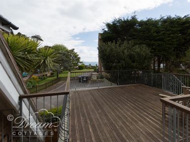 A wooden balcony with metal railings overlooking a garden and trees at Redcliff View Lodge in Weymouth