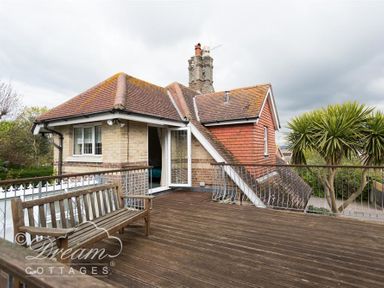 A rooftop wooden deck with a wooden bench and metal railing attached to a house with tiled roofs and open door at Redcliff View Lodge in Weymouth